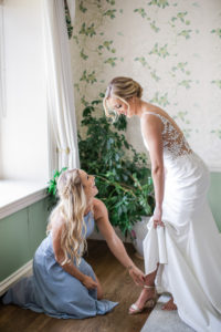 A bridesmaid helps the bride put on her shoes before her wedding at Hamilton Farm Golf club in New Jersey. Photo by Kelly Kollar Photography.