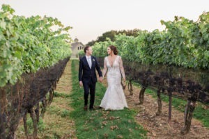 A bride and groom walk through the vineyard on their wedding day at Jonathan Edwards Winery. Photo by Kelly Kollar Photography.