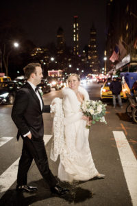 A bride and groom on their wedding day crossing the street at night in Manhattan on the way to New York Athletic Club. Photo by Kelly Kollar Photography.